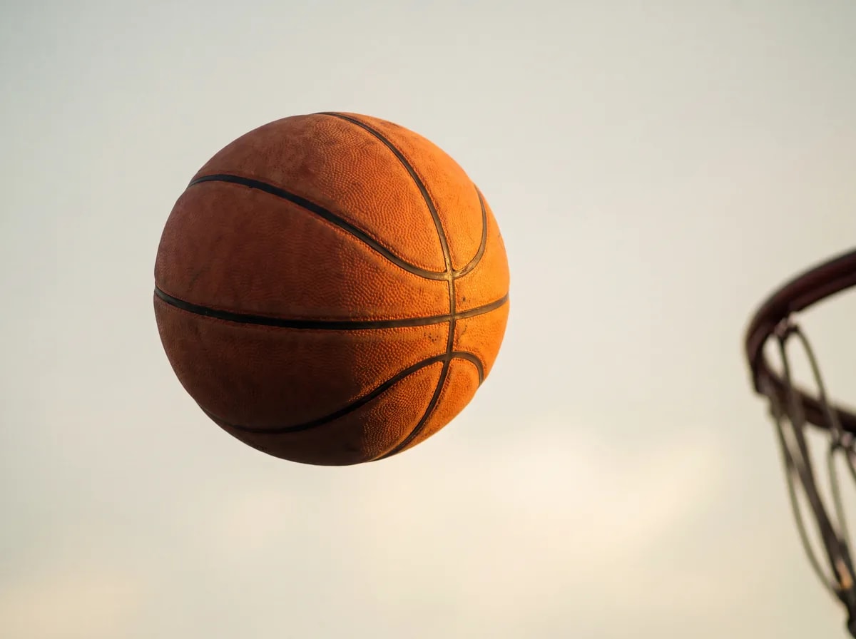 Un balón de baloncesto en el aire, a punto de llegar al aro, contra un cielo claro.